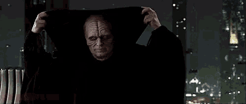 a man in a hooded cloak is standing in front of a window in a dark room .