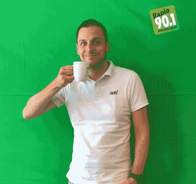 a man holding a coffee mug in front of a green background that says radio 90.1