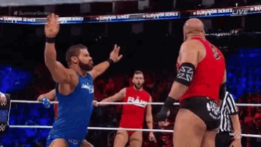 a man in a blue tank top is standing in a wrestling ring with a man in a red shirt .