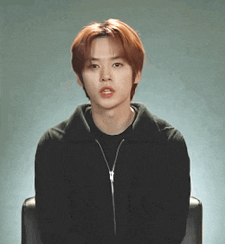a young man with red hair is wearing a black jacket and sitting in a chair .