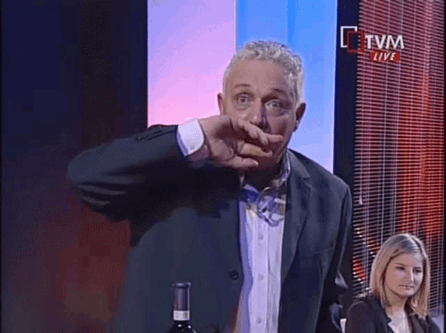 a man in a suit and bow tie stands in front of a tvm live screen