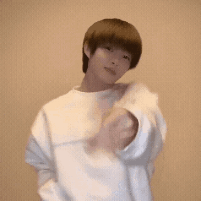 a young man is wearing a white sweater and making a heart shape with his hand .