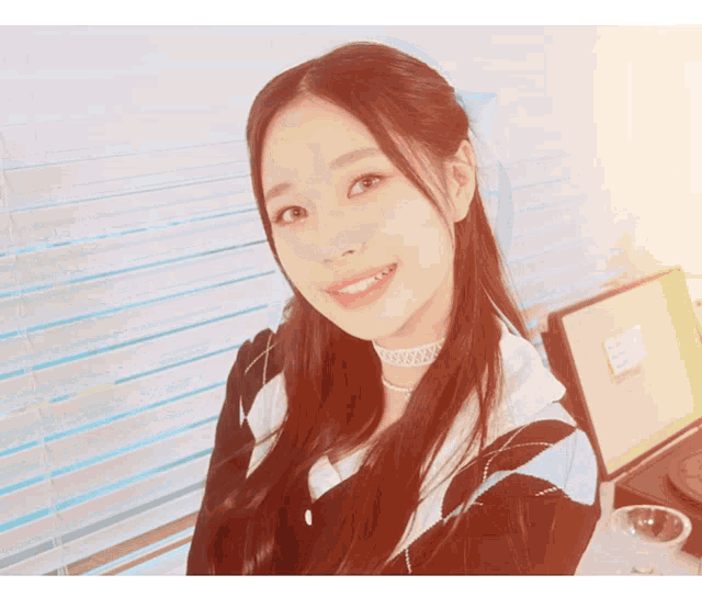 a woman wearing a choker is smiling in front of a window with blinds
