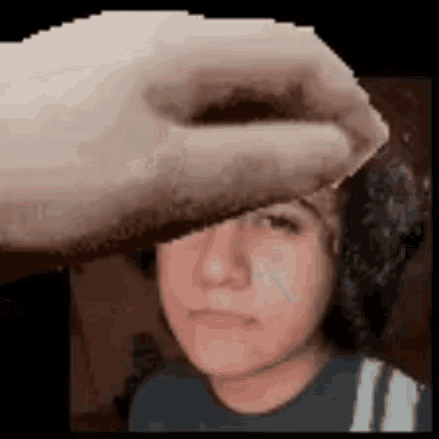 a hand is touching a young boy 's face in a pixelated image .