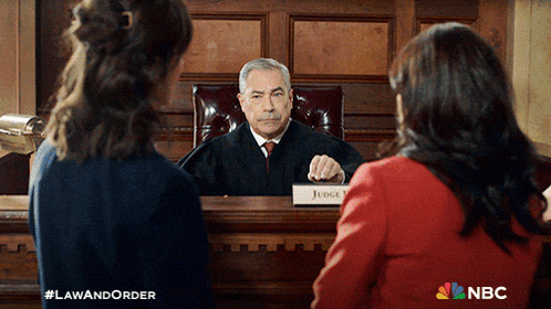 a judge sitting in a courtroom with two women behind him and a sign that says judge