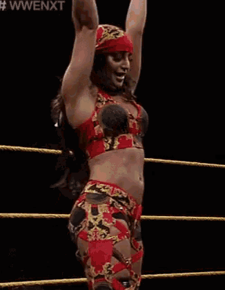 a woman is standing in a wrestling ring with her arms in the air while a referee looks on .