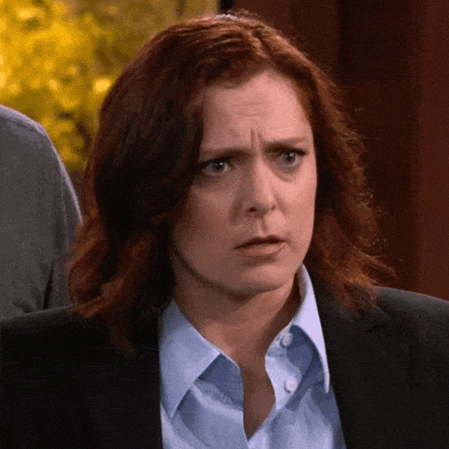 a woman with red hair is wearing a suit and a blue shirt and making a funny face .