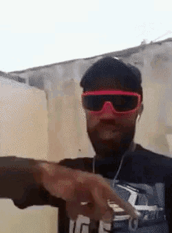 a man wearing sunglasses and a hat is pointing at something .