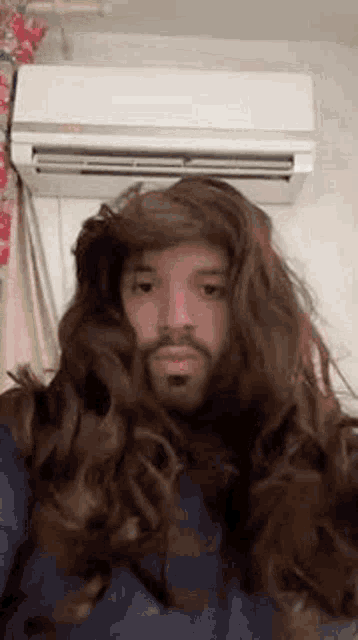 a man wearing a wig and a beard is standing in front of a wall air conditioner .