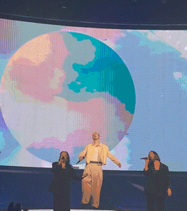 a group of people singing in front of a large screen with a globe on it