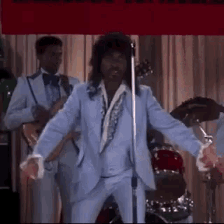 a man in a blue suit is dancing in front of a microphone in a room .