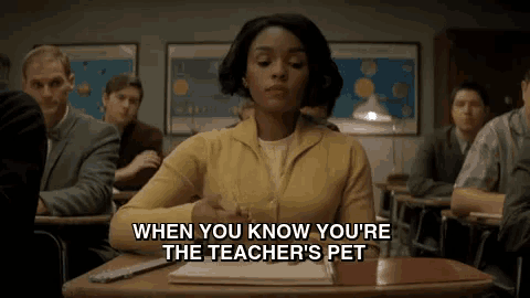 a woman in a yellow sweater is sitting at a desk in a classroom with other people .
