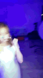 a little girl in a white dress is dancing in front of a blue wall .