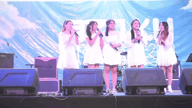a group of girls singing on a stage with a roland amplifier in the back