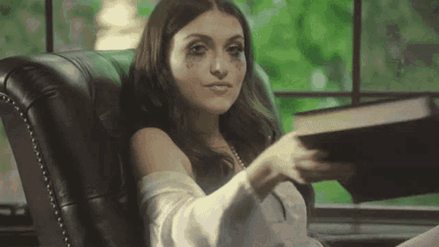 a woman is sitting in a leather chair holding a book