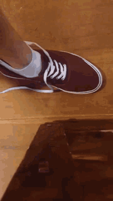 a person wearing a pair of red shoes with white laces on a wooden floor