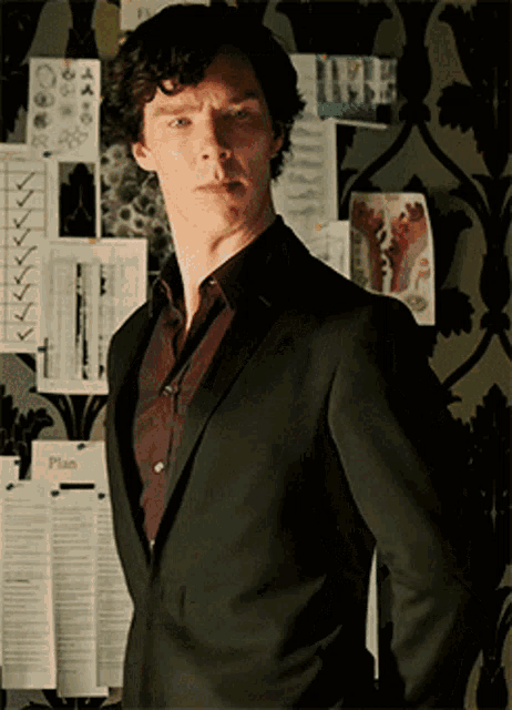a man in a suit is standing in front of a wall with papers pinned to it that say plan