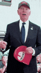a man in a suit and tie is holding a red hat that says " i must "