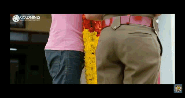a man in a pink shirt is standing next to a man in a tan uniform with goldmines written on the bottom