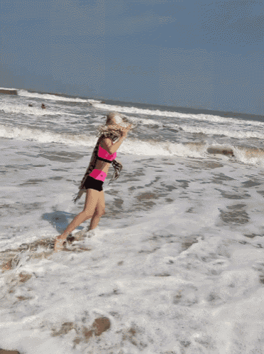 a woman in a pink top and black shorts stands in the ocean
