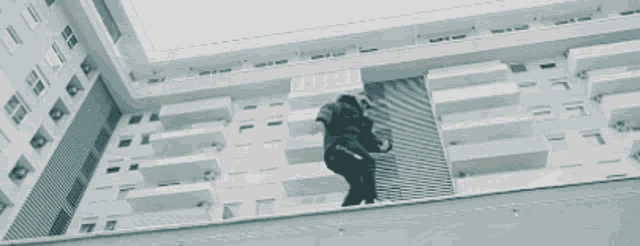 a man in a black jacket and pants is standing in front of a building .