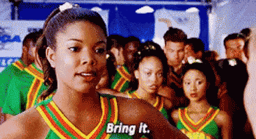 a group of cheerleaders are standing next to each other in a gym and one of them is talking to the camera .