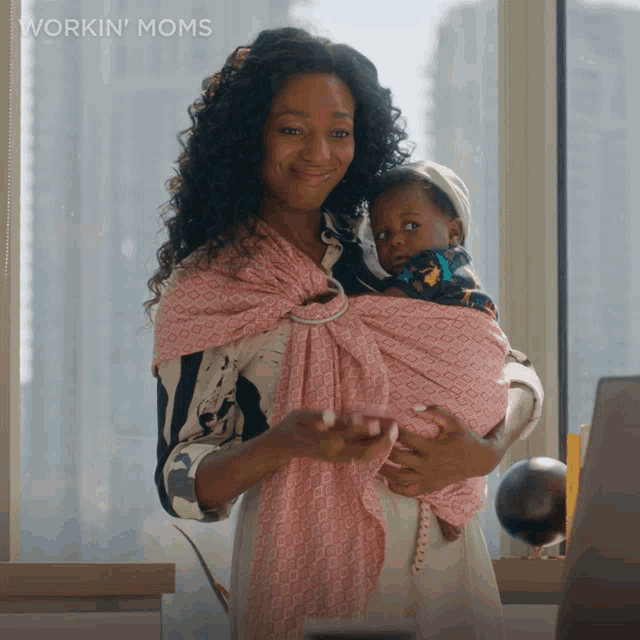 a woman is holding a baby in a pink sling with the words workin ' moms written on the bottom