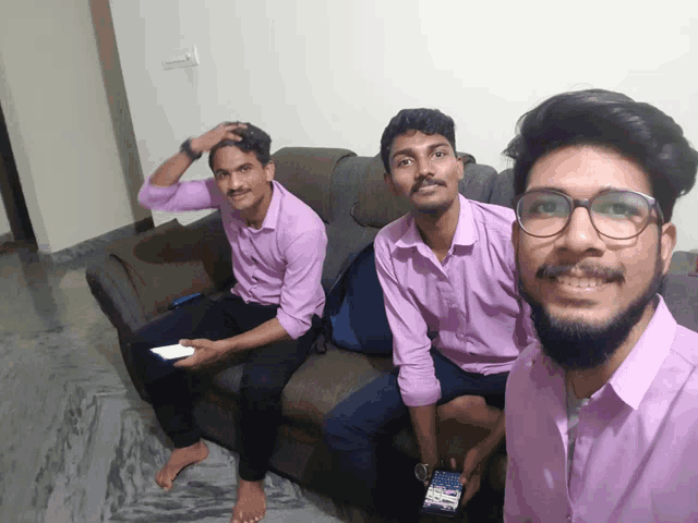 three young men are sitting on a couch and one of them is holding a cell phone