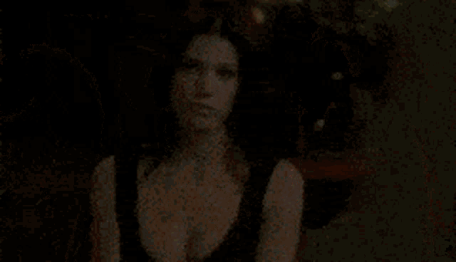 a woman in a black tank top is looking at the camera with her breasts visible .