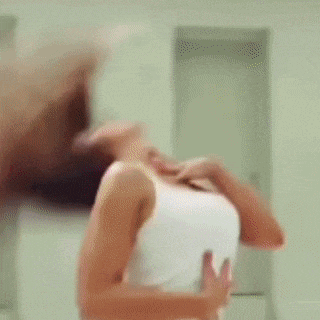 a woman is dancing in front of a mirror in a white tank top .