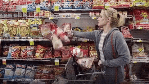 a woman is shopping in a grocery store and picking up chips .