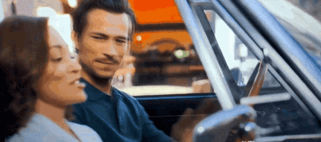 a man is driving a car with a woman sitting in the back seat looking out the window .