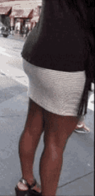a woman wearing a black shirt and a white skirt is walking down the street