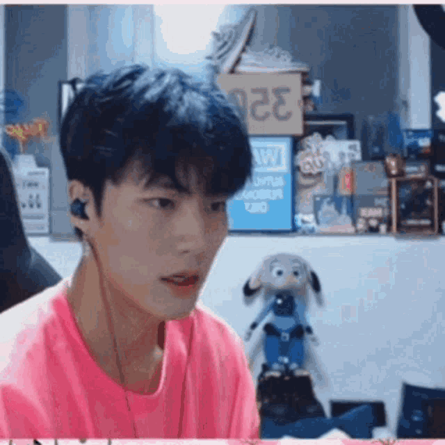 a man wearing headphones and a pink shirt is sitting in front of a computer screen .