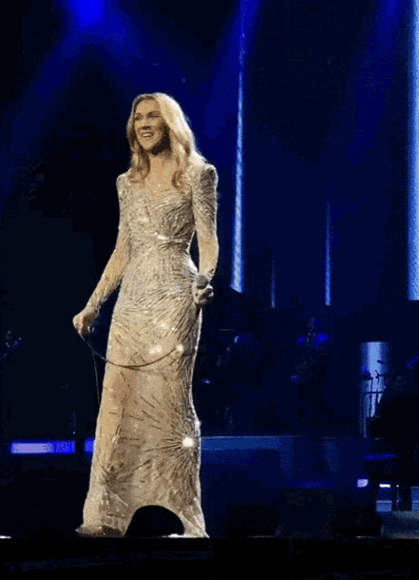 a woman in a long white dress is singing into a microphone on a stage