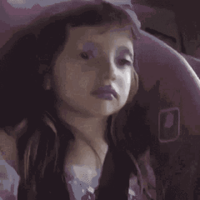 a little girl with purple lipstick on her lips is looking out of a window .