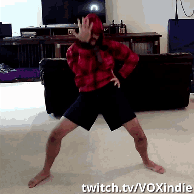 a man in a red plaid jacket and black shorts is dancing on twitch.tv