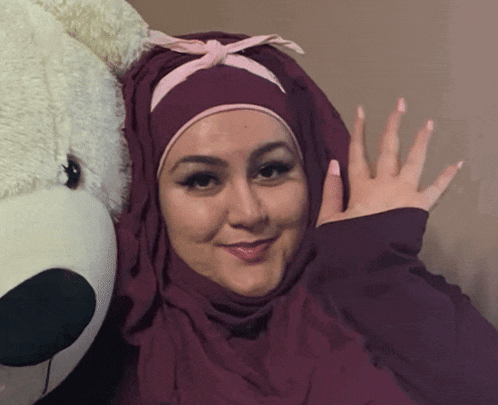 a woman in a hijab is standing next to a stuffed animal