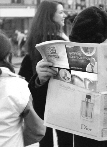 a man is reading a newspaper with an ad for dior homme on it