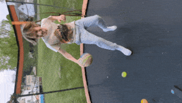 a young boy in a t-shirt with a dinosaur on it is playing with a ball on a trampoline