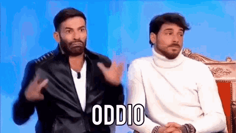 two men are sitting next to each other and one of them is wearing a turtleneck sweater and a leather jacket .