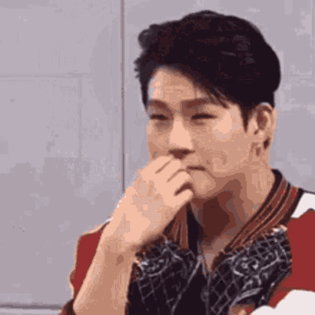 a man is covering his mouth with his hand while wearing a red and white shirt .
