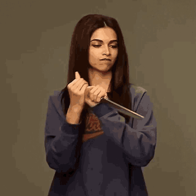 a woman in a blue shirt is holding a knife between her hands .