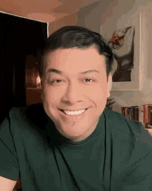a man in a green shirt is smiling with a picture of a woman in the background