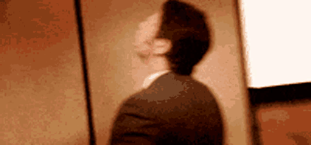 a man in a suit is standing in front of a wall and looking up at something .
