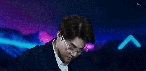 a young man wearing glasses is standing in front of a neon background .