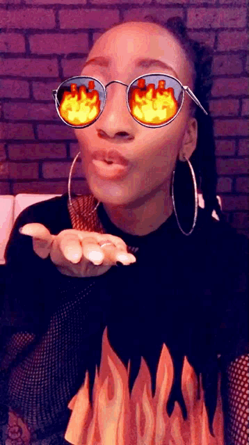 a woman wearing a shirt with flames on it and sunglasses with flames on them blowing a kiss