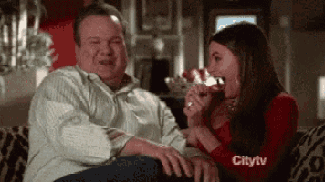 a man and a woman are sitting on a couch drinking wine and laughing .