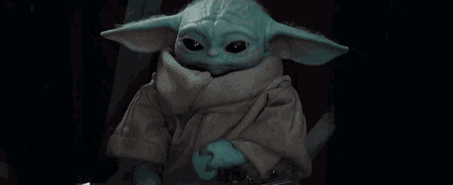 a baby yoda is holding a sword and looking at the camera in a dark room