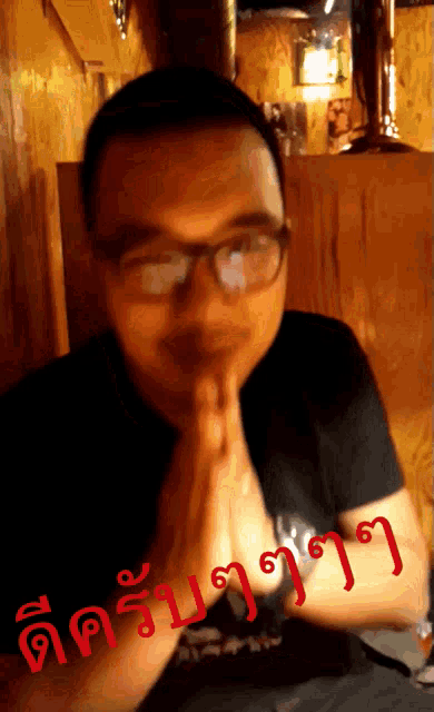 a man wearing glasses and a black shirt is praying in front of a sign in red letters